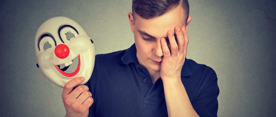 Hombre triste con una máscara de payaso, simbolizando la dualidad emocional en el trastorno bipolar