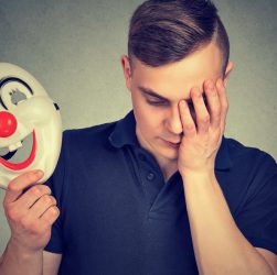 Hombre triste con una máscara de payaso, simbolizando la dualidad emocional en el trastorno bipolar